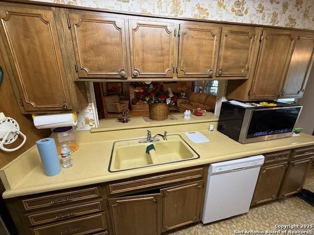 kitchen featuring wallpapered walls, dishwasher, a sink, stainless steel microwave, and light countertops