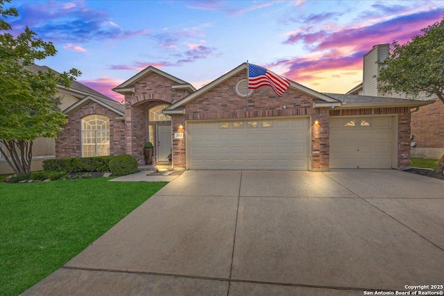 view of front of property featuring a yard, driveway, brick siding, and an attached garage
