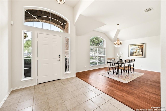entryway featuring an inviting chandelier, light tile patterned floors, visible vents, baseboards, and lofted ceiling