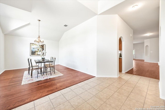 dining area featuring light tile patterned flooring, arched walkways, vaulted ceiling, a chandelier, and baseboards