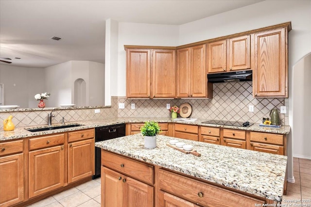 kitchen with a sink, black appliances, under cabinet range hood, light tile patterned floors, and light stone countertops
