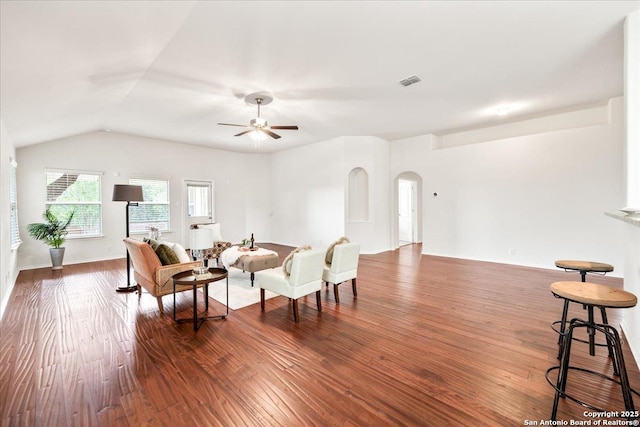 living room featuring lofted ceiling, dark wood-type flooring, visible vents, ceiling fan, and arched walkways