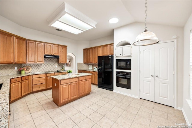 kitchen with under cabinet range hood, light tile patterned floors, light stone counters, black appliances, and tasteful backsplash