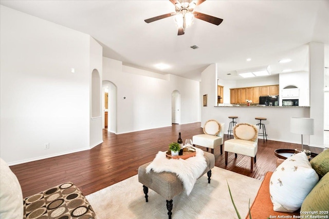 living area with recessed lighting, visible vents, ceiling fan, arched walkways, and dark wood-style floors