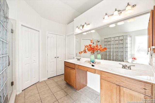 full bathroom featuring double vanity, tile patterned floors, a tile shower, and a sink