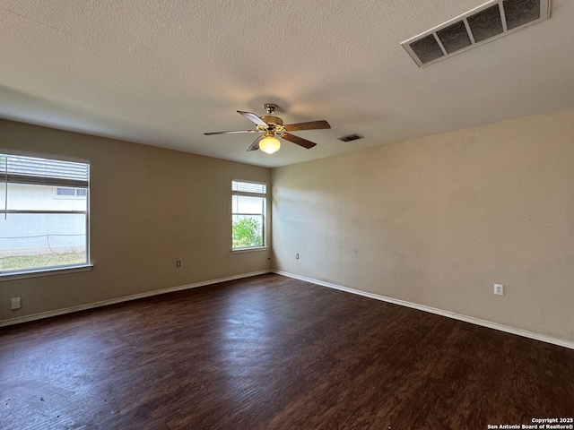 empty room featuring visible vents, a ceiling fan, and dark wood-type flooring