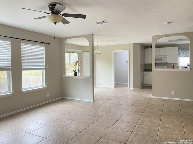 empty room with light tile patterned floors, visible vents, baseboards, ceiling fan, and arched walkways