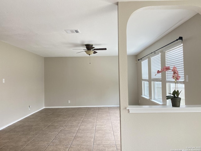 empty room featuring visible vents, tile patterned flooring, arched walkways, a ceiling fan, and baseboards