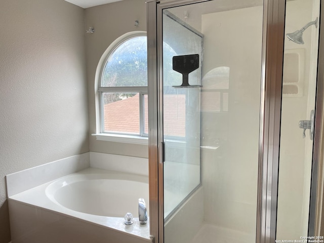 full bath with a bath, a textured wall, a shower stall, and plenty of natural light