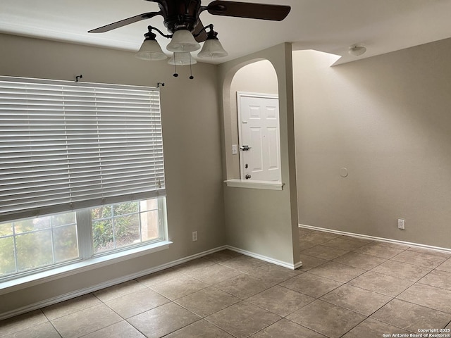 tiled empty room featuring a ceiling fan, baseboards, and arched walkways