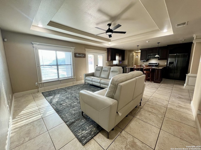 living room featuring a ceiling fan, visible vents, baseboards, a raised ceiling, and light tile patterned flooring