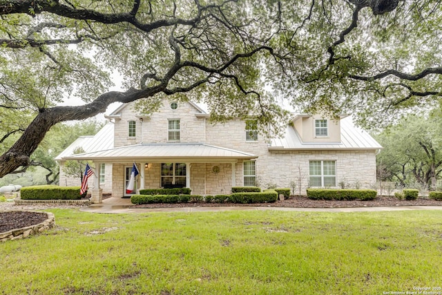 country-style home with stone siding, covered porch, metal roof, a front yard, and a standing seam roof