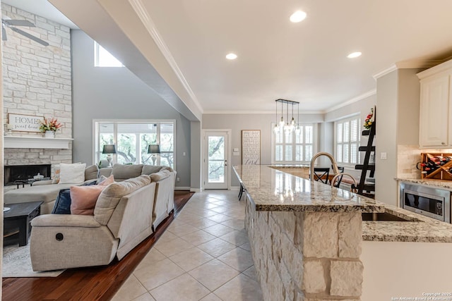 kitchen with light stone counters, an inviting chandelier, light tile patterned flooring, stainless steel microwave, and a fireplace