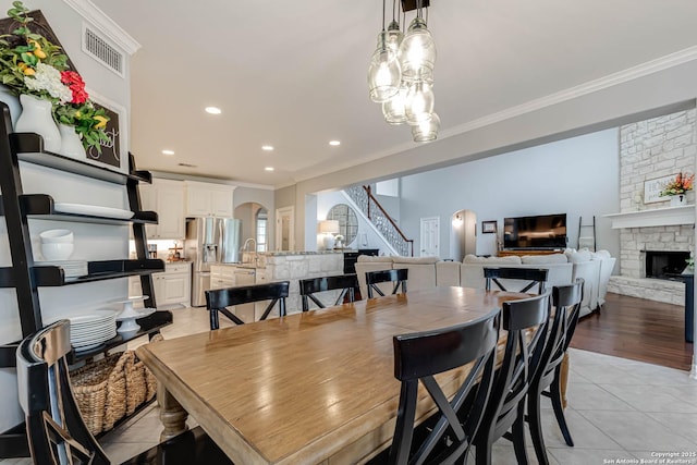 dining space with a stone fireplace, crown molding, stairway, and arched walkways