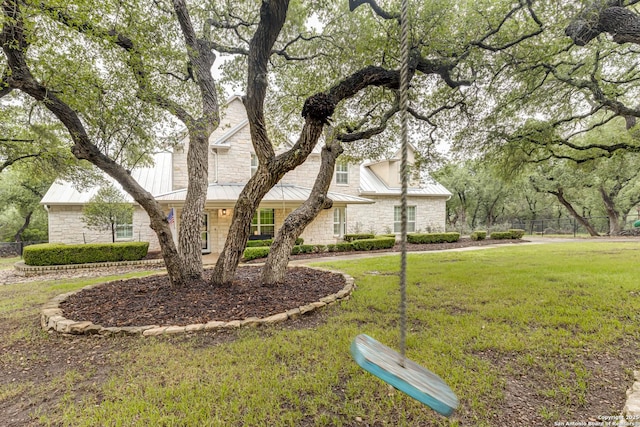 view of front of home featuring stone siding, fence, a front yard, and a standing seam roof