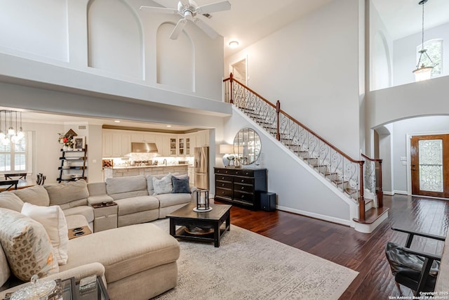 living area with dark wood-style flooring, a towering ceiling, arched walkways, and stairs