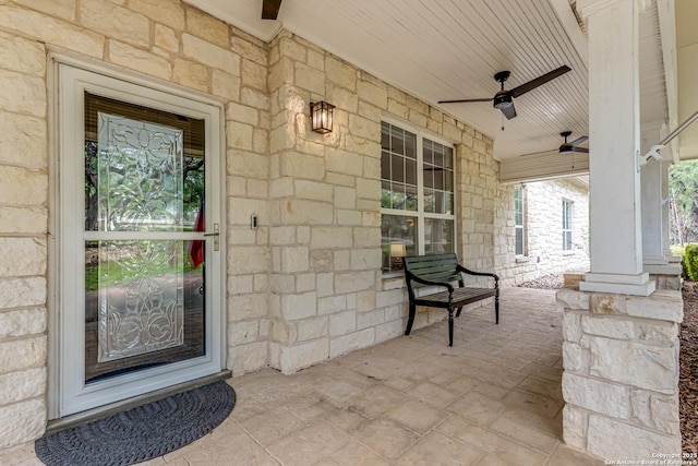 entrance to property with a ceiling fan, stone siding, and covered porch