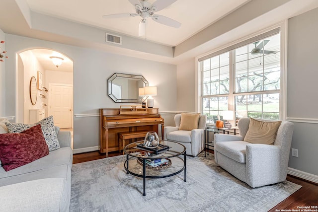 living room with wood finished floors, a ceiling fan, visible vents, baseboards, and arched walkways