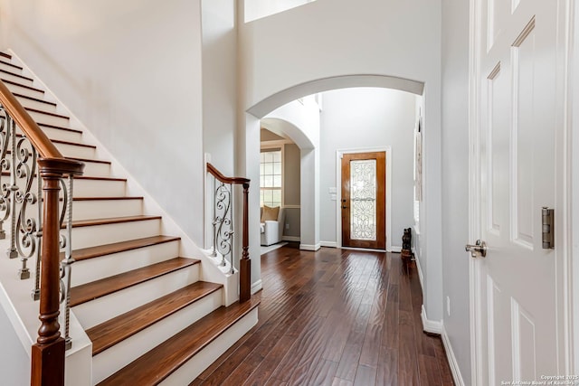 foyer featuring dark wood-style flooring, a towering ceiling, baseboards, arched walkways, and stairs