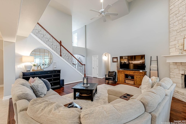 living room with a ceiling fan, a towering ceiling, a stone fireplace, arched walkways, and stairs