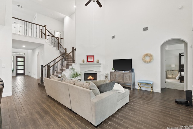 living area featuring a towering ceiling, ceiling fan, dark wood-type flooring, arched walkways, and baseboards