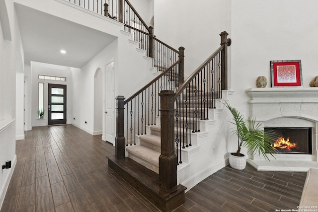 entryway with wood finished floors, arched walkways, baseboards, stairs, and a high ceiling