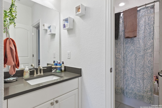 full bath with a textured wall, vanity, and curtained shower