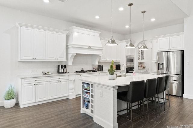 kitchen featuring appliances with stainless steel finishes, dark wood-style floors, white cabinets, a center island with sink, and backsplash
