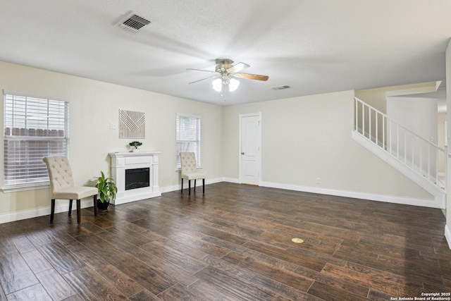 living area featuring stairs, a ceiling fan, wood finished floors, baseboards, and a fireplace with raised hearth