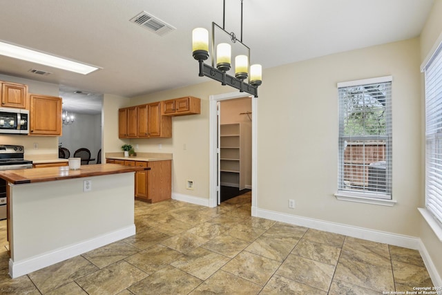 kitchen featuring stainless steel appliances, a chandelier, hanging light fixtures, wood counters, and brown cabinets
