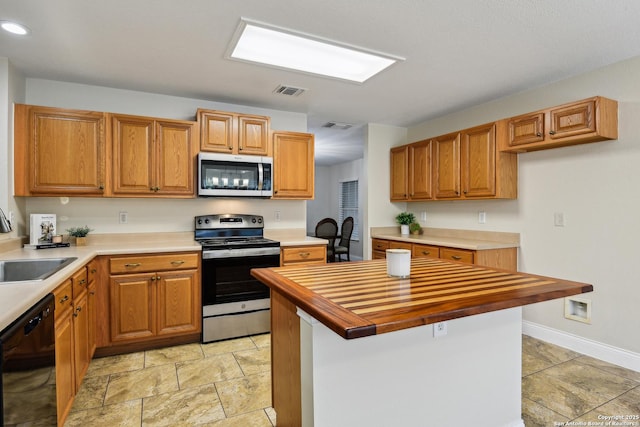 kitchen featuring stainless steel appliances, a sink, butcher block countertops, brown cabinetry, and a center island