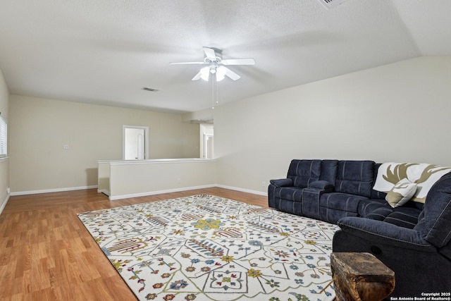 living room featuring wood finished floors, a ceiling fan, baseboards, a textured ceiling, and lofted ceiling