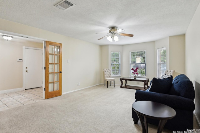 living area featuring light colored carpet, a ceiling fan, baseboards, and a textured ceiling
