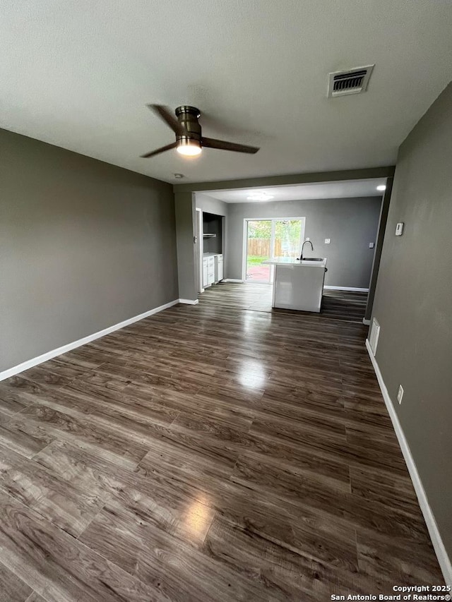 unfurnished living room featuring a ceiling fan, dark wood finished floors, and baseboards