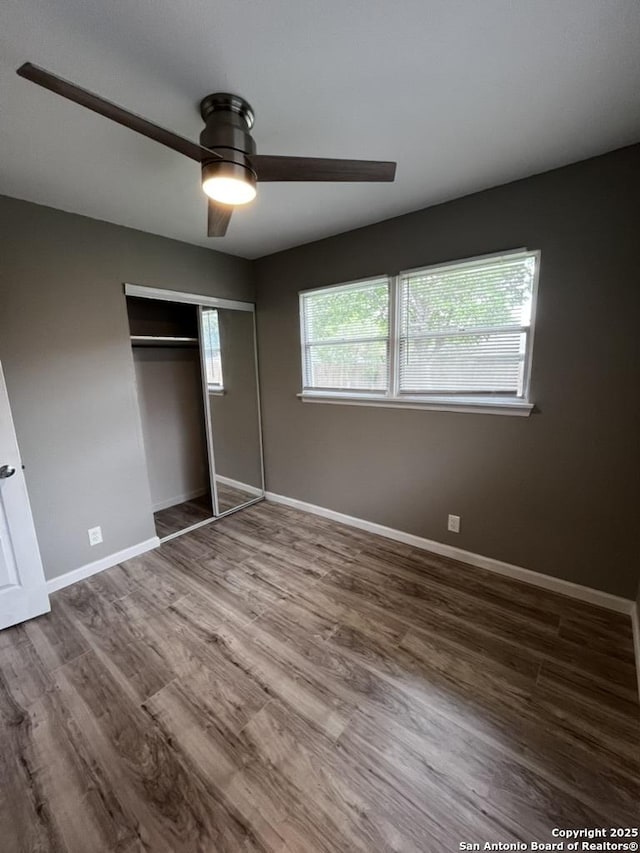 unfurnished bedroom featuring wood finished floors, baseboards, a closet, and ceiling fan