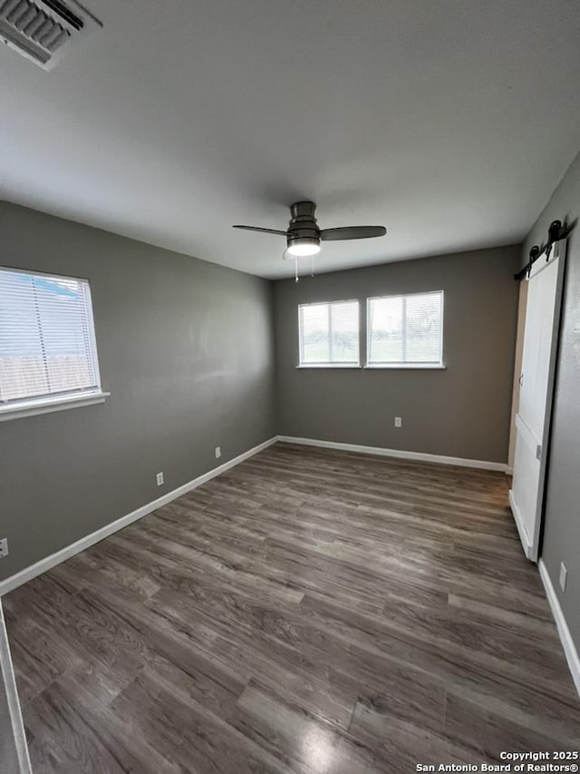 unfurnished room with ceiling fan, a barn door, dark wood-type flooring, and baseboards