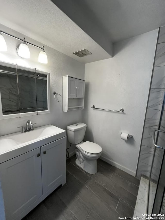 bathroom with toilet, vanity, baseboards, a shower with door, and a textured ceiling