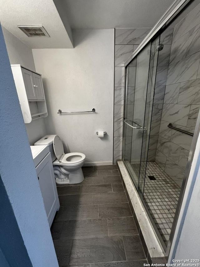 full bathroom featuring toilet, a stall shower, wood finish floors, a textured ceiling, and vanity
