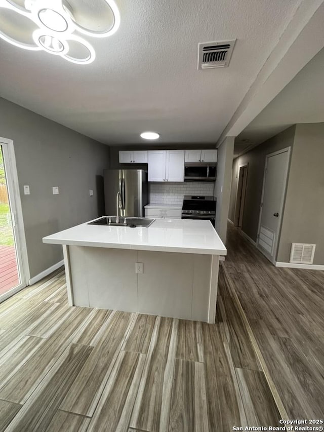 kitchen with appliances with stainless steel finishes, a sink, wood finished floors, white cabinets, and a spacious island