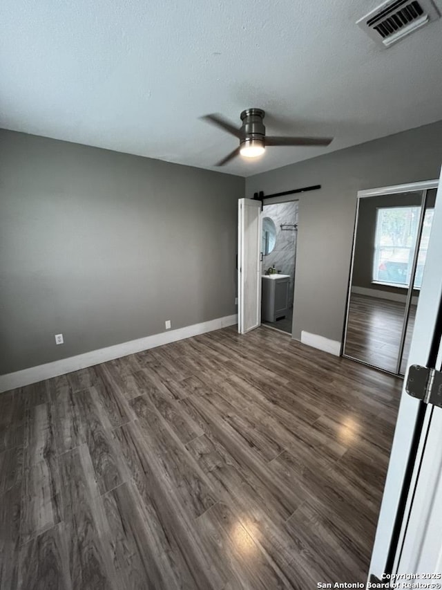 unfurnished bedroom featuring dark wood finished floors, baseboards, ceiling fan, a textured ceiling, and a barn door