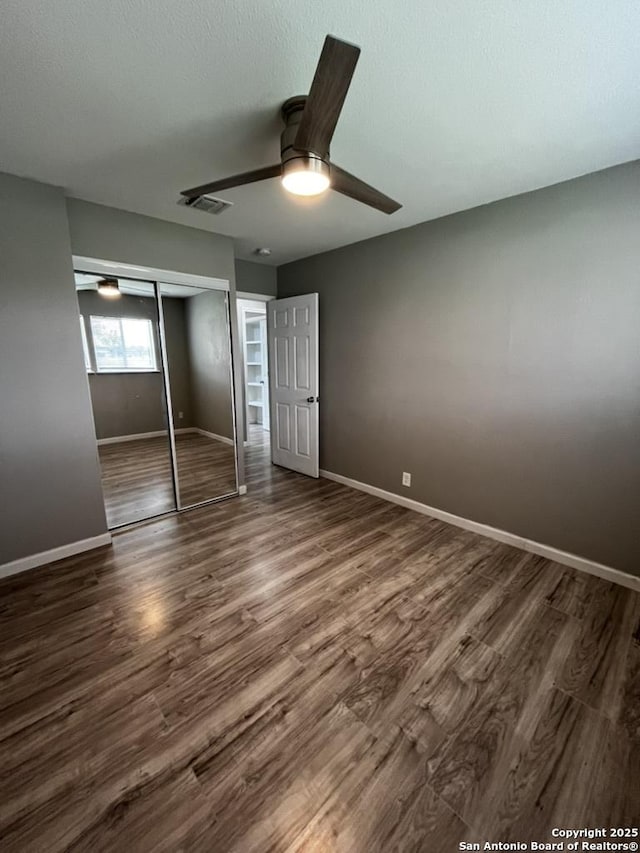 unfurnished bedroom featuring a closet, dark wood-style floors, baseboards, and ceiling fan