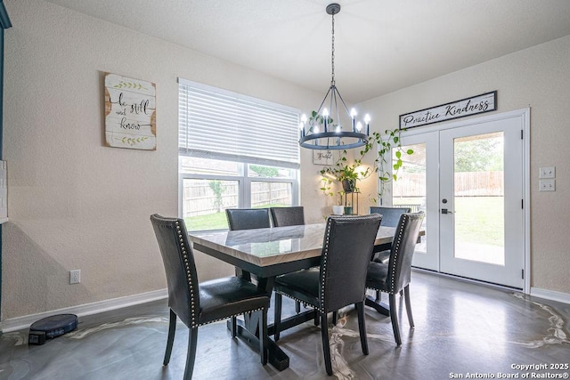 dining room with a chandelier, plenty of natural light, concrete flooring, a textured wall, and baseboards