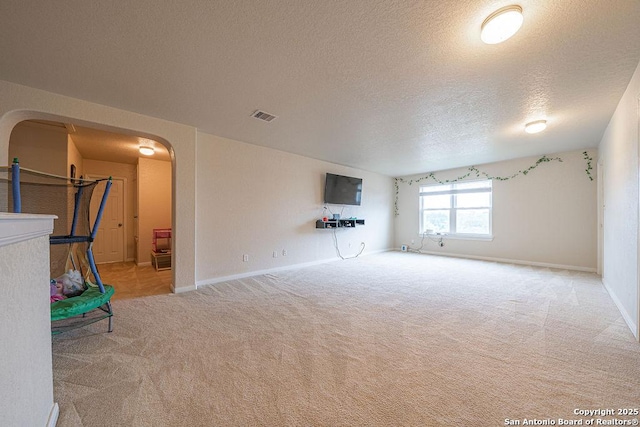 unfurnished living room with arched walkways, carpet floors, a textured ceiling, and baseboards