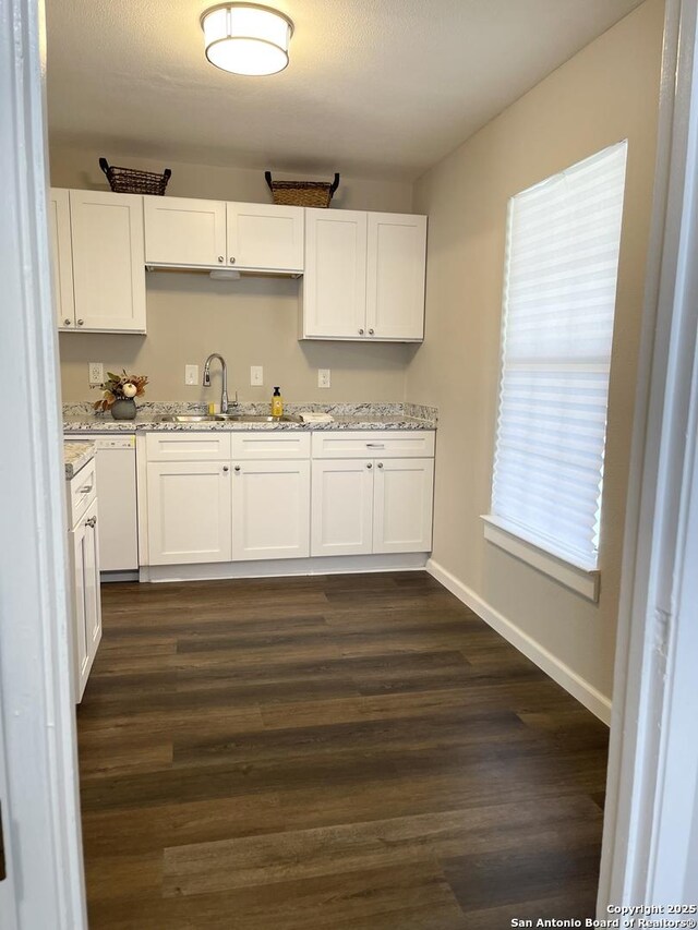 kitchen with a sink, white cabinetry, light stone countertops, white dishwasher, and dark wood-style flooring