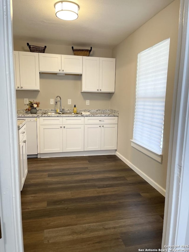 kitchen with a sink, white cabinetry, light stone countertops, white dishwasher, and dark wood-style flooring