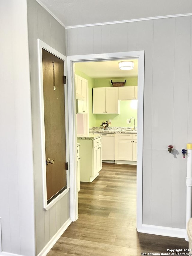 hall with crown molding, light wood finished floors, a sink, and a decorative wall