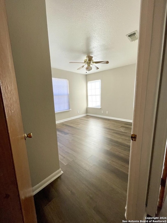 unfurnished room featuring baseboards, a ceiling fan, dark wood finished floors, and a textured ceiling