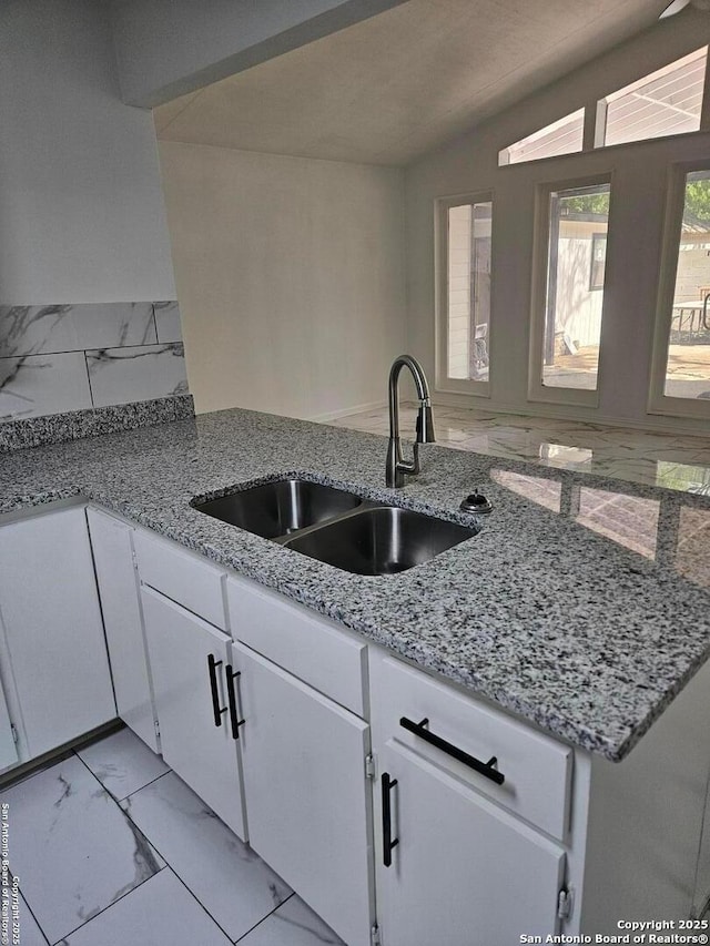kitchen featuring a sink, light marble finish floors, white cabinets, light stone countertops, and vaulted ceiling