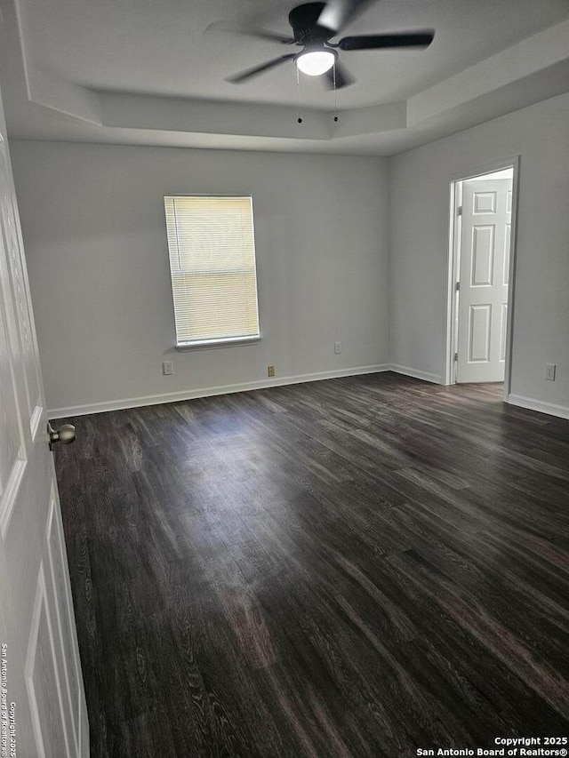 spare room featuring dark wood-type flooring, ceiling fan, a raised ceiling, and baseboards