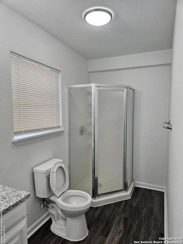 bathroom featuring wood finished floors, a shower stall, toilet, baseboards, and vanity